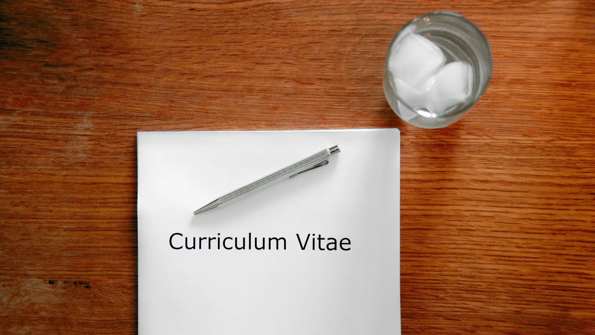 Tavolo con bicchiere, penna e carta con scritto "Curriculum vitae"